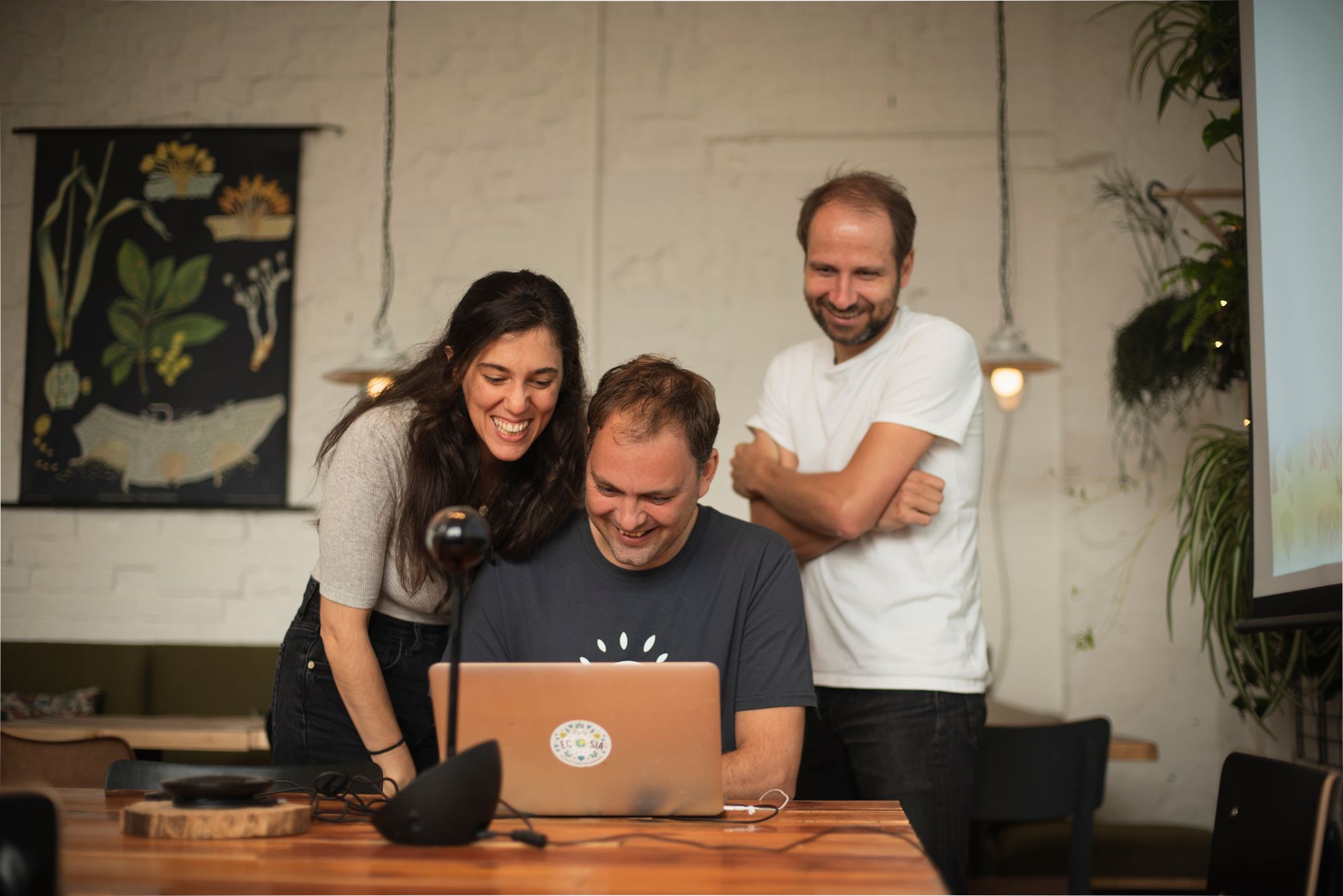 Three team members look onto a laptop, smiling. 