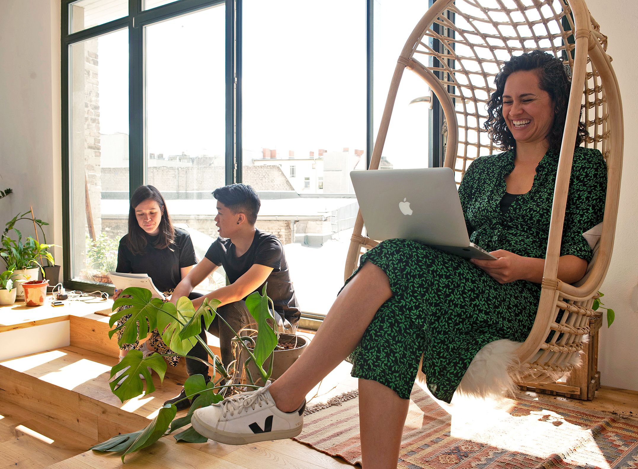 A smiling colleague works on her laptop in the sun, in a swing chair